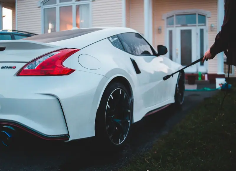 White sports car being rinsed in a home driveway at dusk during a mobile detail