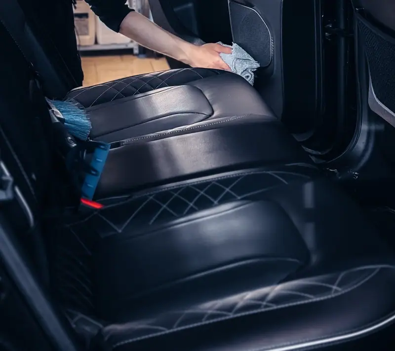 Microfiber towel wiping a door panel beside quilted leather seats