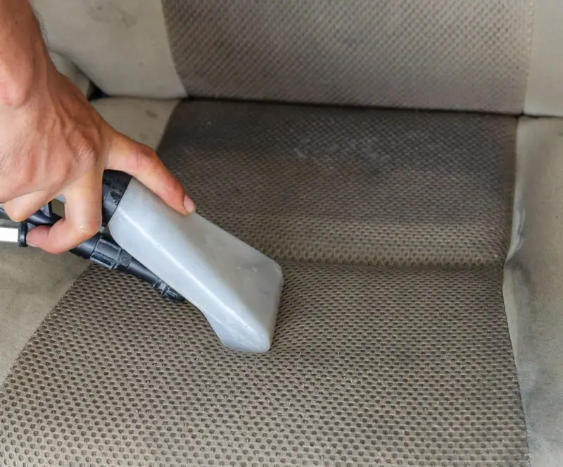 Extractor nozzle lifting dirt out of a fabric car seat during upholstery shampoo