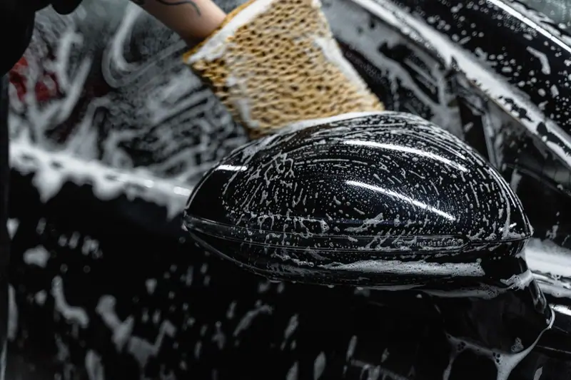 Soapy wash mitt on a black side mirror during a two-bucket hand wash