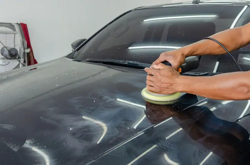 Machine polisher with a foam pad on a dark hood under bright work lights